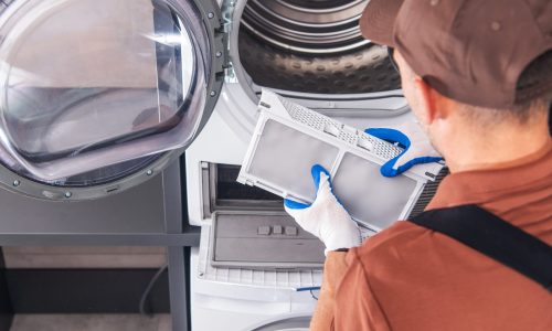 Caucasian Appliances Technician in His 40s Cleaning Washer and Dryer Filter. Home Appliances Maintenance.