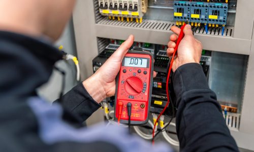 Worker measuring and repairing an electrical system panel in a factory